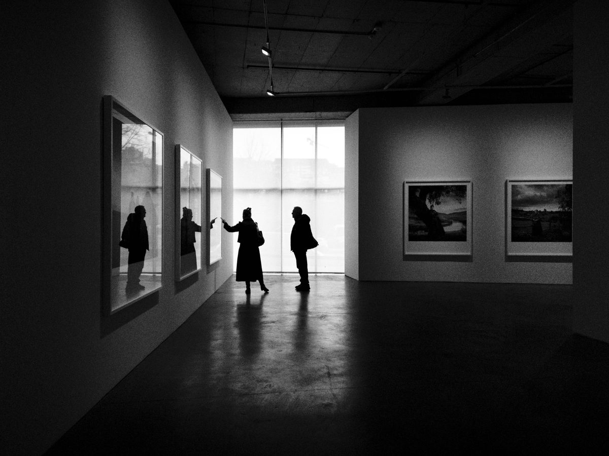 Deux visiteurs devant des photographies encadrées, dans une galerie baignée de lumière